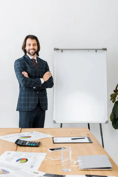 Jeune homme souriant agent d'assurance debout avec les bras croisés près du tableau blanc dans le bureau — Photo de stock