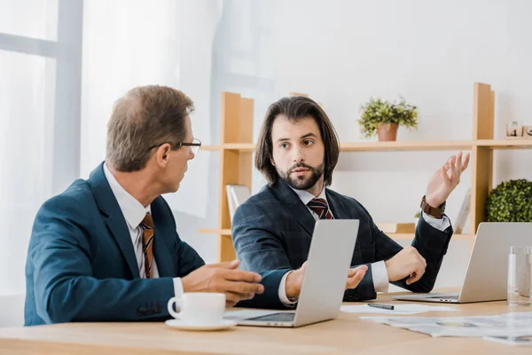 Dos hombres adultos sentados en la mesa y hablando en la oficina de seguros - foto de stock