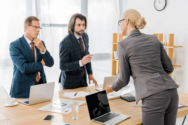 Trabajadores de seguros de pie cerca de la mesa y teniendo discusión en la oficina - foto de stock