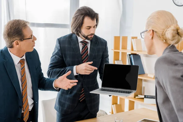 Giovane agente assicurativo maschile in piedi con i lavoratori e che indica il computer portatile in carica — Foto stock