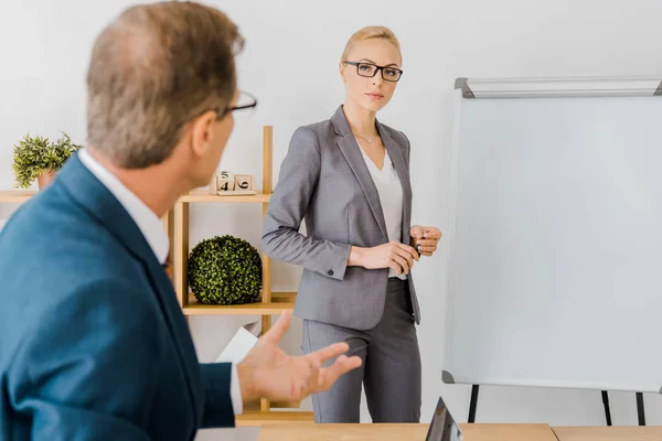 Adult man talking to young woman near white board in office — Stock Photo