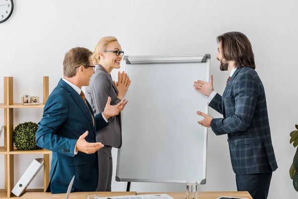 Улыбающиеся офисные работники, указывающие на белую доску на заседании — стоковое фото