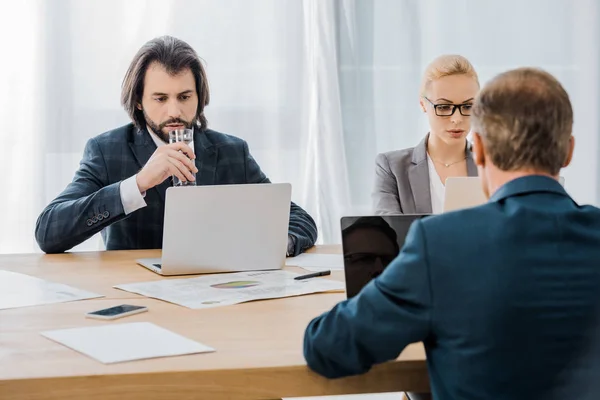 Uomini d'affari seduti a tavola con i computer portatili in ufficio — Foto stock