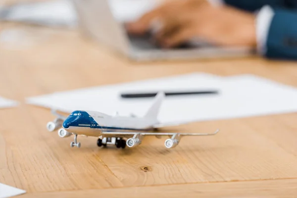 Toy airplane at wooden table with office worker using laptop on blurred background — Stock Photo
