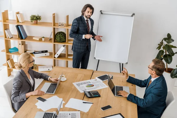 Young businessman standing near board and speaking at meeting in office — Stock Photo