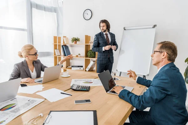 Young businessman standing near board and speaking at meeting in office — Stock Photo