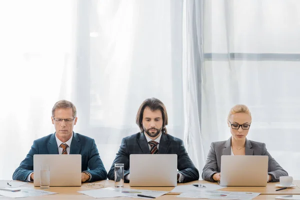 Trabajadores de seguros sentados a la mesa y usando computadoras portátiles en la oficina - foto de stock