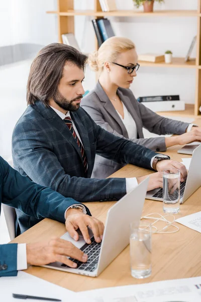 Trabajadores de seguros sentados a la mesa y usando computadoras portátiles en la oficina - foto de stock