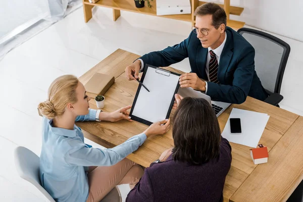 Adult insurance agent in glasses showing contract to young couple in office — Stock Photo