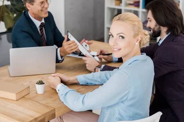 Jeune femme souriante regardant la caméra tandis que l'homme signe un contrat avec un agent d'assurance — Photo de stock