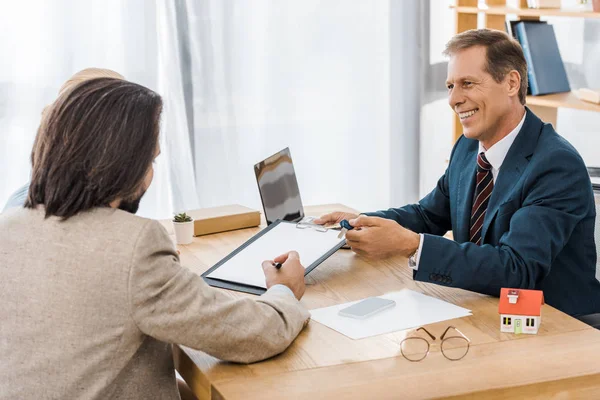 Взрослый улыбающийся страховой агент показывает контракт с человеком в офисе — стоковое фото