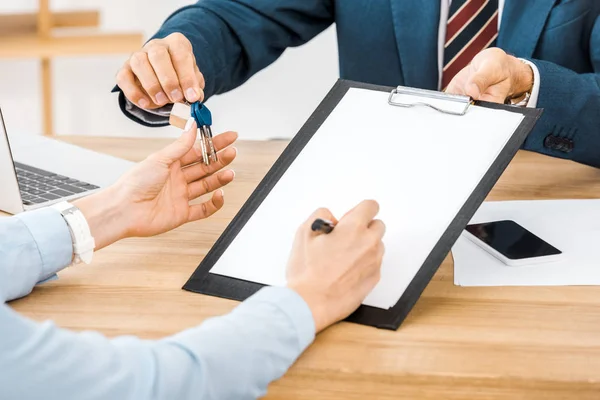 Insurance agent giving keys and contract for signing on clipboard to woman — Stock Photo