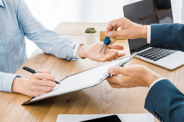 Versicherungsvertreter hält Schlüssel in der Hand, während Frau Vertrag auf Klemmbrett unterzeichnet — Stockfoto