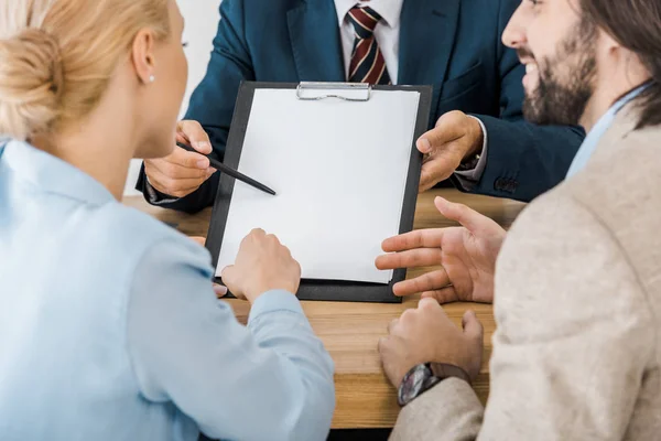 Businessman showing contract on clipboard to couple — Stock Photo