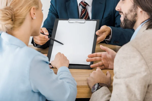 Geschäftsmann zeigt Paar Vertrag auf Klemmbrett — Stockfoto