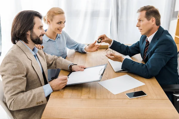 Insurance agent giving key to woman while man signing papers — Stock Photo