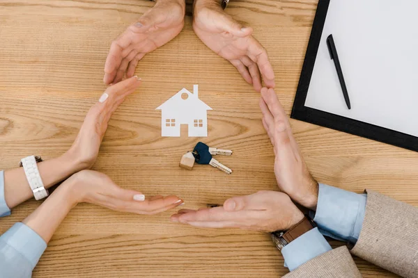 People making circle with hands on wooden table with paper house and keys inside — Stock Photo