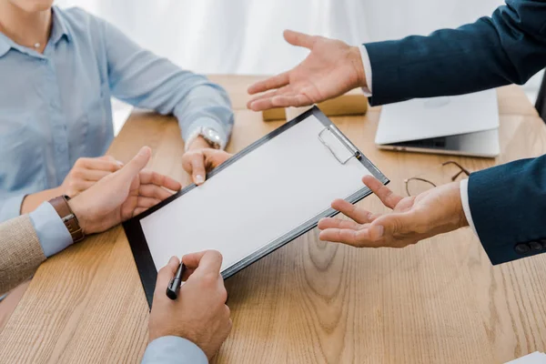 Couple signing contract on clipboard with insurance agent at wooden table — Stock Photo