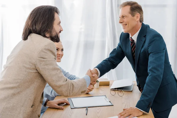 Hombre feliz y agente de seguros estrechando las manos en la oficina - foto de stock