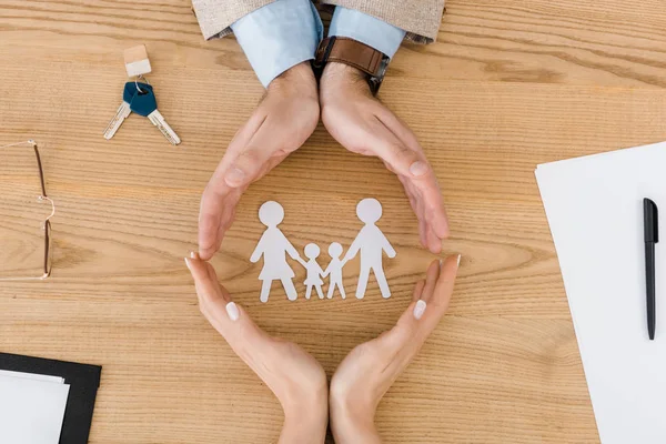 Pareja haciendo círculo con las manos en la mesa de madera con gente de papel en el interior, seguro familiar - foto de stock