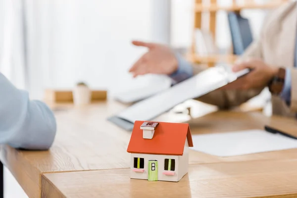 Modello di casa su tavolo in legno con persone sfocate sullo sfondo — Foto stock