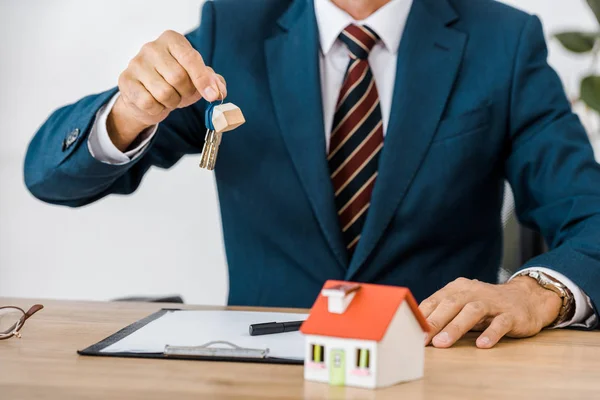 Insurance agent holding keys with house model on table — Stock Photo