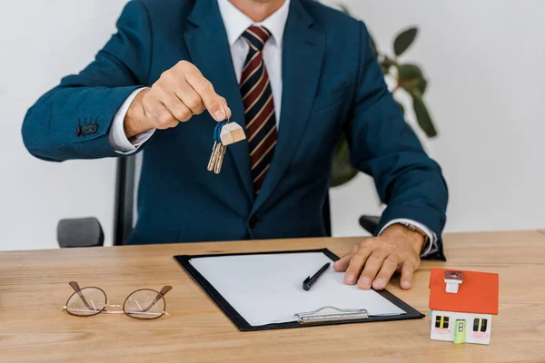Agent d'assurance tenant les clés avec modèle de maison et lunettes sur la table — Photo de stock