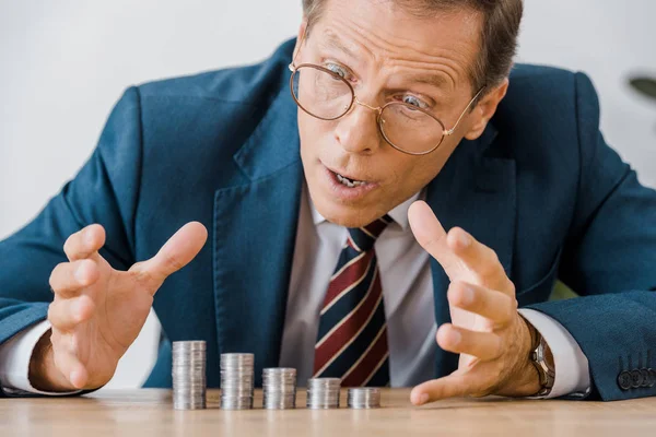 Empresário surpreso olhando para moedas de prata na mesa de madeira — Fotografia de Stock