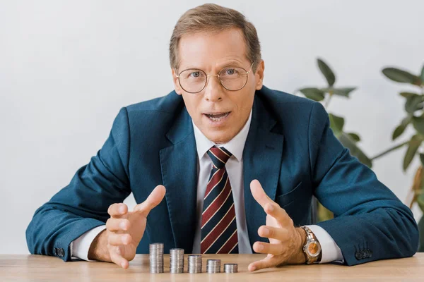 Surprised businessman in glasses looking at silver coins at wooden table — Stock Photo