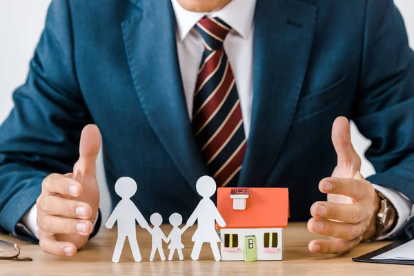 Manos masculinas en la mesa de madera con la familia de papel cortado y modelo de casa - foto de stock