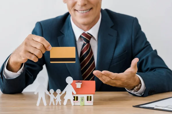 Hombre de negocios con tarjeta de crédito con modelo de casa y la familia de papel cortado en mesa de madera - foto de stock
