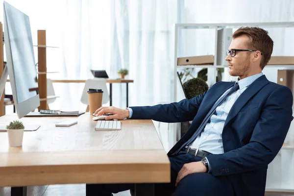 Vista lateral de hombre de negocios en gafas que trabajan en la mesa con monitor de computadora en la oficina moderna - foto de stock