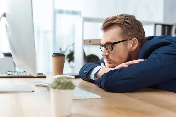 Focused businessman in eyeglasses sitting at table with computer monitor in office — Stock Photo