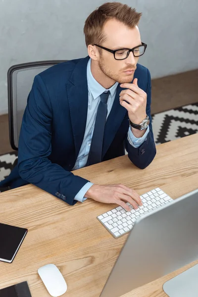 High angle view of businessman in eyeglasses working at table with computer monitor in modern office — Stock Photo