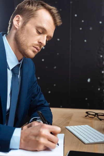 Homme d'affaires concentré écriture dans le manuel à la table avec smartphone dans le bureau moderne — Photo de stock