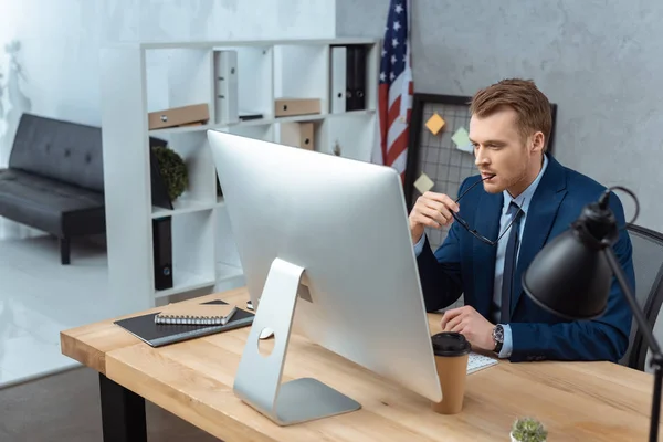 Pensativo hombre de negocios con anteojos sentado a la mesa con ordenador y smartphone en la oficina moderna - foto de stock