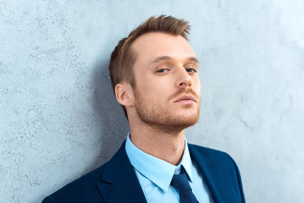 Portrait of handsome businessman looking at camera near wall in office — Stock Photo