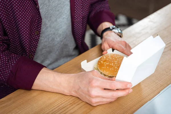 Imagem cortada de empresário almoçando com hambúrguer à mesa no escritório moderno — Fotografia de Stock