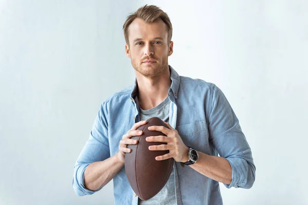 Confident handsome man holding rugby ball and looking at camera near wall — Stock Photo