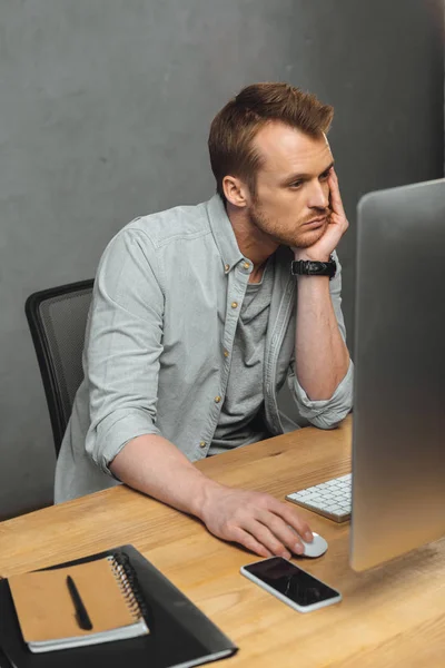 Jeune homme d'affaires travaillant à table avec ordinateur et smartphone au bureau — Photo de stock