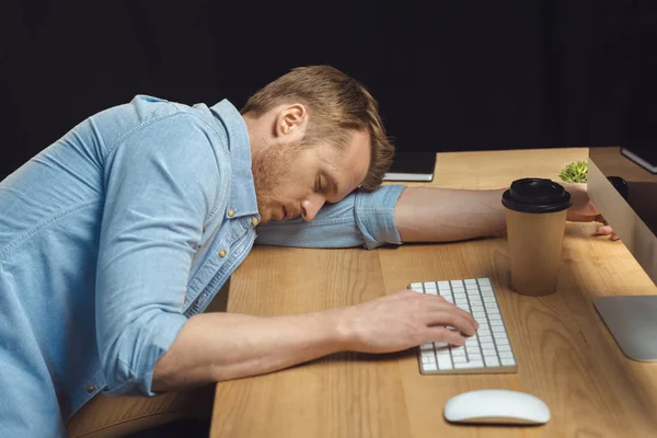 Tired businessman sleeping at table with computer and paper coffee cup during night time in office — Stock Photo