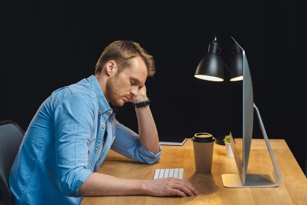 Vista lateral do empresário dormindo à mesa com computador e xícara de café de papel durante a noite no escritório — Fotografia de Stock
