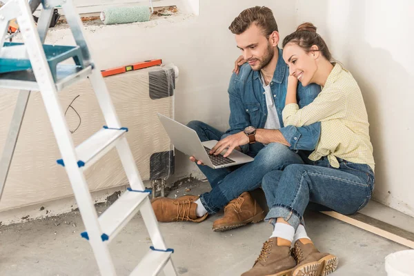 Vista de ángulo alto de la pareja joven usando el ordenador portátil mientras está sentado en el suelo en la casa nueva - foto de stock