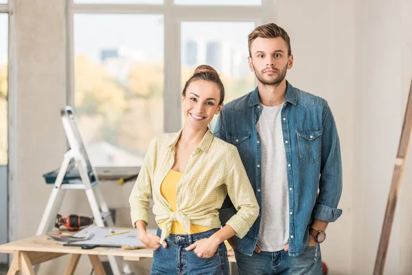 Happy young couple standing together and smiling at camera in new dwelling — Stock Photo