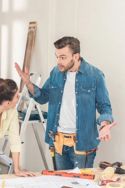 Emotivo giovane uomo gesticolando e litigando con la ragazza durante la riparazione della casa — Foto stock
