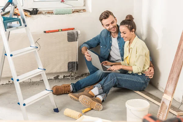 Feliz joven pareja usando el ordenador portátil durante la renovación en la nueva casa - foto de stock