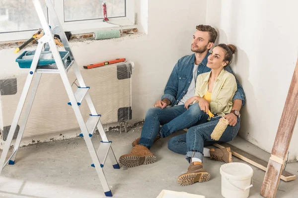 Vue grand angle de jeune couple coûteux assis ensemble sur le sol et regardant loin à la nouvelle maison — Photo de stock