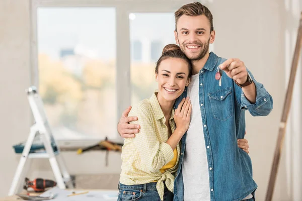 Feliz joven pareja sosteniendo la llave de nuevo apartamento y sonriendo a la cámara — Stock Photo