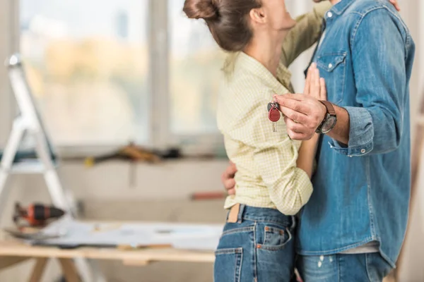 Schnappschuss von jungem Paar, das sich umarmt und Schlüssel aus neuer Wohnung hält — Stockfoto