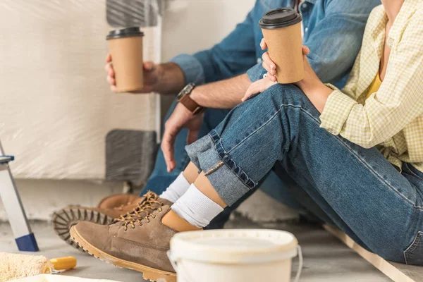 Plan recadré de jeune couple tenant du café pour aller et assis sur le sol pendant l'amélioration de la maison — Photo de stock